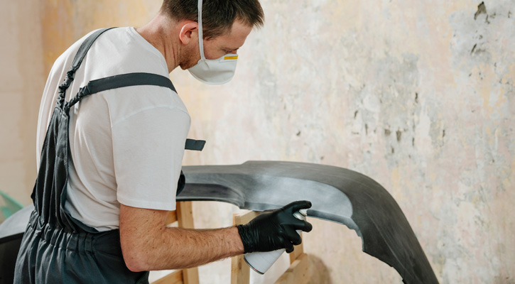 worker wearing work clothes paiting a car part