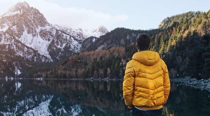 man wearing down jacket in front of a mountain lake