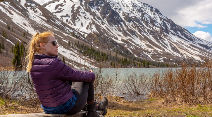 woman sitting down in front of a mountain lake