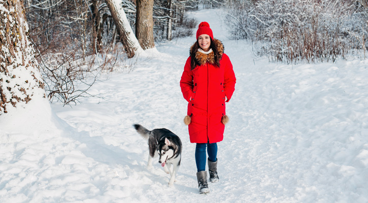 woman wearing red winter parka walking on snow with her dog