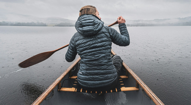 woman wearing down jacket paddling on a lake